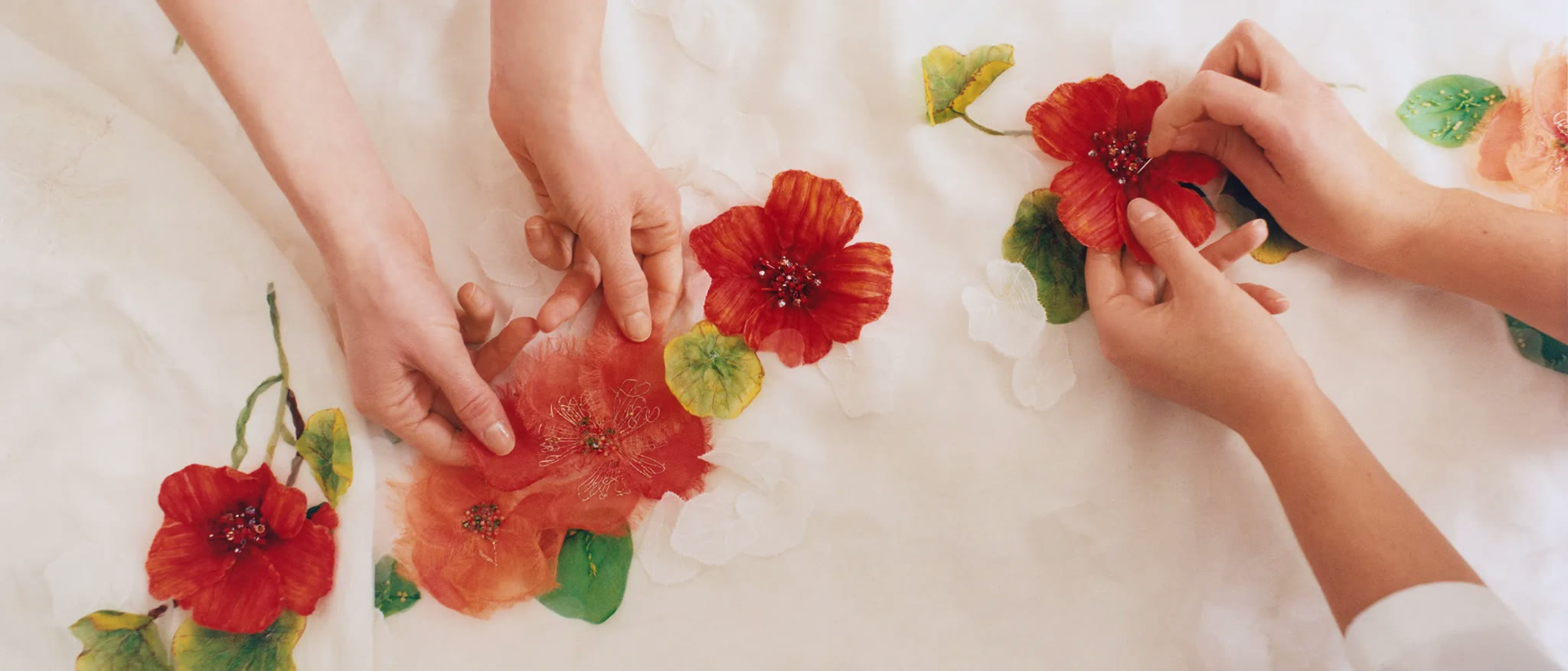 Hands setting worked silk flowers onto organza in the Adorsoin atelier